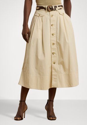 Jupe midi en coton beige avec un devant à boutons, des plis et deux poches avant, associée à une ceinture marron à motifs et des talons strappy.