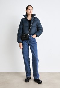 Marineblå pufferjakke med høy krage, kombinert med lyse straight-leg jeans. Svart mini håndveske med detaljer i sølvkjede og svarte platåstøvler.