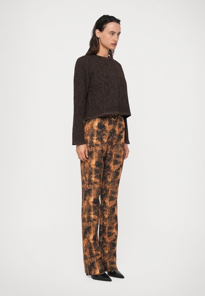 Maglione marrone a maglia con motivo testurizzato e maniche lunghe, abbinato a pantaloni arancioni e neri con motivo. Scarpe nere con punta appuntita.