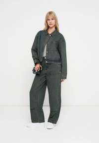 Temnozeleni jeans jakna z ujemajočimi se širokimi hlačami. Ima žep na prsih, svetlo šivanje in obrabljen videz. V kombinaciji z belimi supergami.