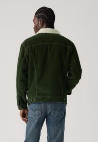 Green corduroy jacket with a cream sherpa collar, featuring a relaxed fit and side vents. Back view shows textured fabric and seams.
