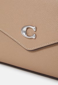 Světle béžová texturovaná kožená kabelka s kovovým logem C, bílým prošíváním na klopě a hladkým, kontrastním lemem.