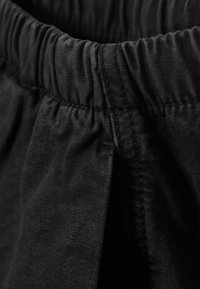 Musta tekstuuriga pinnaga lühikesed püksid, millel on elastne vöökoht ja voltidega disainiline detail, mis võimaldab mugavat liikumist.