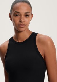 Fekete bordás ujjatlan trikó magas nyakkal, sima textúrával és testhezálló sziluettel. Egyszerű és sokoldalú stílus.