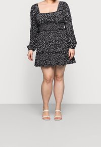 Svart klänning med vit hjärtprint, fyrkantig halsringning, långa ärmar, rynkad midja och volangkant. Bärs med vita sandaletter med remmar.