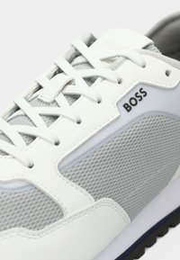 Άσπρο και γκρι αθλητικό παπούτσι με υλικά από δίχτυ και δέρμα, με υφή στην επιφάνεια, εμφανή κορδόνια και μαύρο λογότυπο "BOSS" στο πλάι.