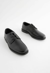 Chaussures en cuir noir avec une texture lisse, bout rond et un laçage à cinq œillets. Style minimaliste avec une semelle profil bas.
