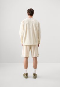 Jasnobeżowa, oversize, długozgięta bluzka z okrągłym dekoltem, zestawiona z pasującymi szortami. Casualowy, sportowy styl, miękka tekstura, minimalne detale.