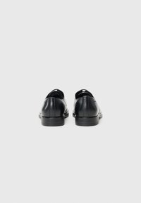 Zwarte leren schoenen met een gladde textuur, ronde neus, lage hak en subtiel merklogo aan de achterkant. Minimalistisch ontwerp zonder zichtbare patronen.