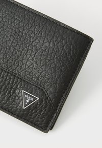 Black leather wallet with a textured surface, featuring a triangular silver logo. Simple design, predominantly dark with minimal accents.