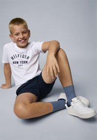 Biela bavlnená tričko s potlačou "HILFIGER NEW YORK CITY" v námorníckej modrej, námornícke šortky, modré ponožky a biele tenisky s námorníckymi akcentami.