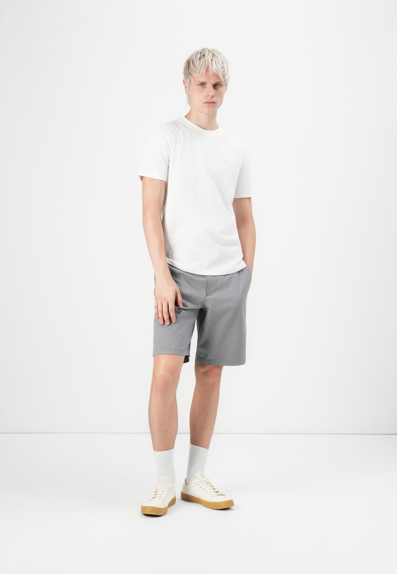 Weißes T-Shirt, graue Shorts, hellfarbene Turnschuhe und graue Socken. Einfaches Design, lockerer Schnitt, kurze Ärmel und ohne Muster.