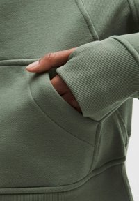 Groene sweatstof trui met een kangoeroezak en geribbelde manchetten. De stof lijkt zacht te zijn met een gestructureerde afwerking en gestikte details.