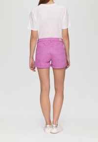 Shorts en denim rose avec ourlets retroussés, poches arrière et une étiquette à la taille, associés à un t-shirt blanc uni et des chaussures légères.
