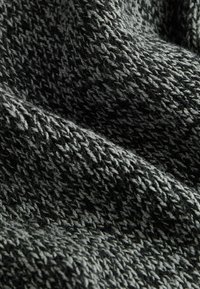 Tissu tricoté dans des nuances de noir et de gris, présentant un motif texturé avec des fils entrelacés et une surface douce et duveteuse.