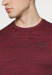 Bordo urheilupaita, jossa on tekstuuripinta, lyhyet hihat ja musta logo rinnassa. Pyöreä kaula-aukko ja tiukka muotoilu.