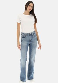 T-shirt bianco a maniche corte abbinato a jeans svasati leggeri a vita alta. Tessuto liscio con cuciture in denim tradizionali e chiusura con bottone.