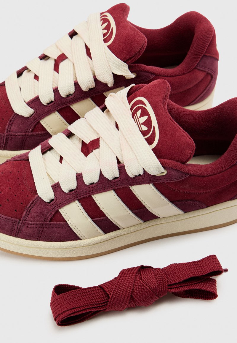 Baskets en suède bordeaux avec des rayures et des lacets crème. Comprend un lacet supplémentaire bordeaux assorti. Logo accentué sur la languette.