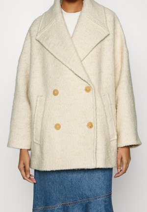 Off-white uldfrakke med dobbeltspænde, brede revers, brune knapper og sidelommer båret over et denimnederdel.