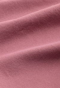 Tissu rose doux avec une texture tissée fine et des plis doux créant des ombres et des reflets subtils.