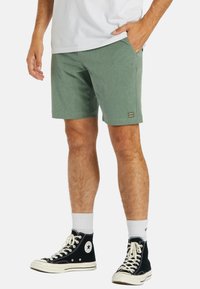 Shorts verts texturés avec un petit patch logo, poches latérales et un ourlet droit, assortis à des baskets montantes noires et des chaussettes blanches.