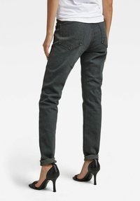 Pantalones vaqueros gris oscuro de corte slim, con costuras claras, dos bolsillos traseros y puños doblados, combinados con sandalias de tacón alto negras.