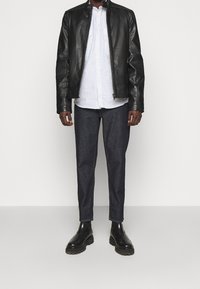 Giacca di pelle nera, camicia a righe bianche e blu, pantaloni di denim scuri e stivali neri con suole spesse; vestibilità comoda, design casual.