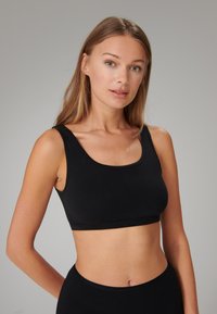 Top corto nero senza cuciture con spalline larghe e scollatura a barca. Materiale morbido ed elasticizzato senza cuciture visibili o dettagli metallici.