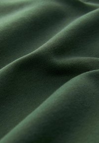 Tela verde oscura con una textura suave, que presenta ligeros pliegues y un acabado suave, mostrando su elasticidad y caída.