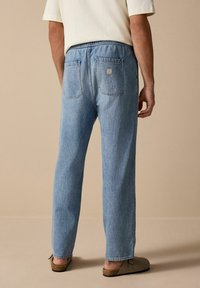 Jeans din denim albastru deschis, cu croi lejer, două buzunare la spate și talie elastică. Țesătura are o textură netedă și un finisaj decolorat.