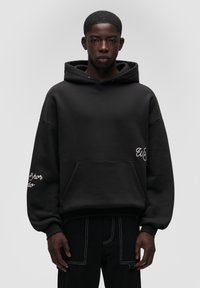 Czarna, oversize bluza z kapturem z przednią kieszenią, haftowanymi detalami na rękawach oraz miękkim, teksturowanym materiałem. Prosty, minimalistyczny design.