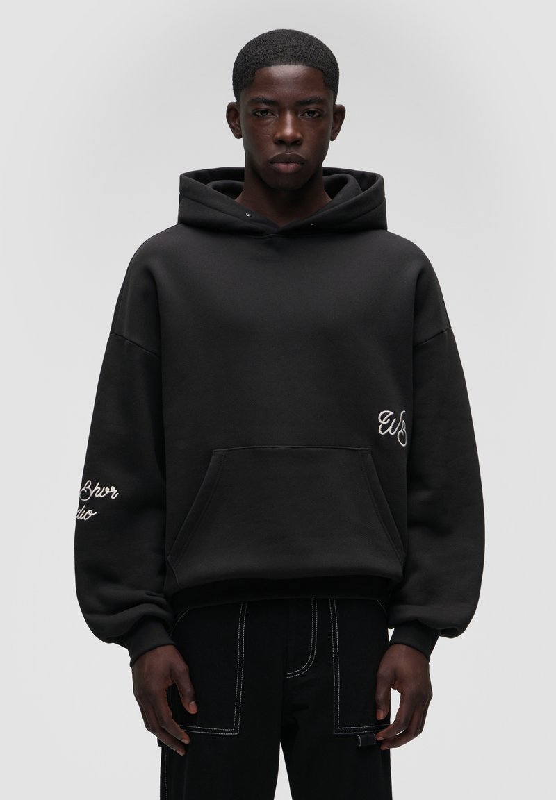 Czarna, oversize bluza z kapturem z przednią kieszenią, haftowanymi detalami na rękawach oraz miękkim, teksturowanym materiałem. Prosty, minimalistyczny design.