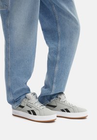 Jasnoszare sneakersy z czarnymi akcentami, z gładką skórzaną cholewką, okrągłym czubkiem i białą gumową podeszwą. Para stylizowana z luźnymi dżinsami.