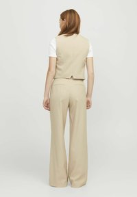 Beige op maat gemaakt gilet en wijde broek, met een gladde textuur en een minimaal ontwerp. De achterkant toont splitdetails op het gilet.