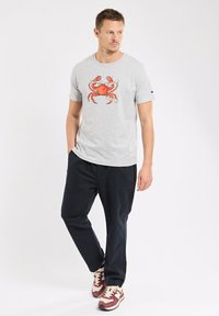 T-shirt en coton gris avec un graphisme de crabe rouge, associé à un pantalon bleu marine foncé et des baskets bordeaux avec des accents blancs.