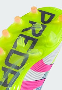 Semelle de crampons de football verte et rose avec six crampons orange, surface texturée et grands lettres noires "ADIDAS" affichées de manière proéminente.