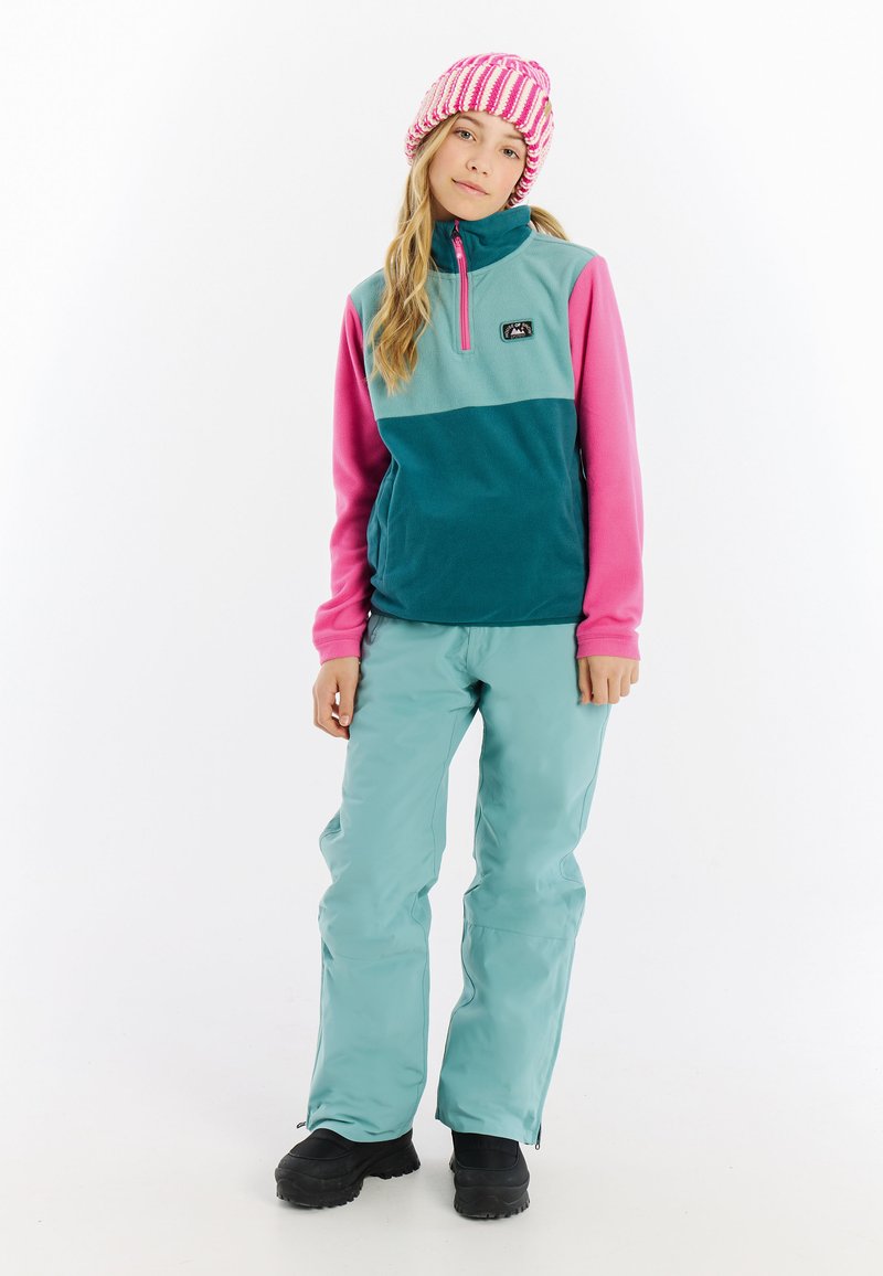 Fleece pullover in teal en roze met een halve rits, gecombineerd met lichtteal broeken en zwarte laarzen. Bevat een logo op de borst.