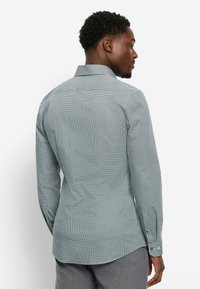 Gemustertes Langarmhemd in Türkis und Weiß, mit klassischem Kragen, Knopfmanschetten und abgerundetem Saum mit strukturierter Oberfläche.