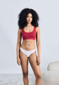 Červený rebrovaný športový podprsenka a biele tangá, ktoré majú priliehavý dizajn s hladkými švami a minimalistickým štýlom.