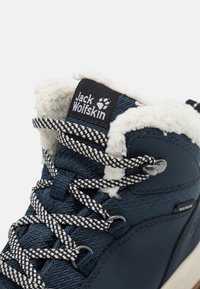 Stivale blu a metà altezza con tessuto texturizzato e foderatura in pelliccia sintetica, lacci con motivo nero e bianco e un'etichetta con logo sul colletto.