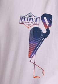 Bílý tričko s grafickým designem stylizovaného plameňáka v purpurových a oranžových odstínech, doplněné logem "PETROL" nahoře.