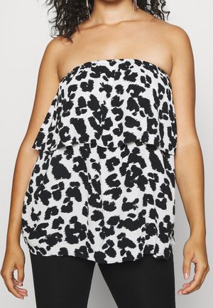 Mujer con top sin tirantes de estampado de leopardo en blanco y negro con detalle de volantes en capas y pantalones negros.