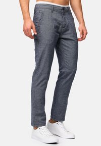 Pantalones tejidos grises con un corte ajustado, que presentan una parte delantera plana, una textura sutil y zapatillas blancas.