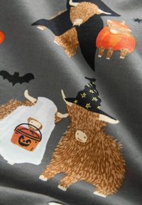 Le tissu présente un fond gris avec des illustrations colorées de vaches des Highlands, de citrouilles et de chauves-souris, utilisant des tons chauds et des designs ludiques.