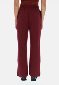 Bordové kalhoty s širokými nohavicemi vyrobené z měkké tkaniny s elastickým pasem; mají hladký povrch a rovný střih až k kotníkům.