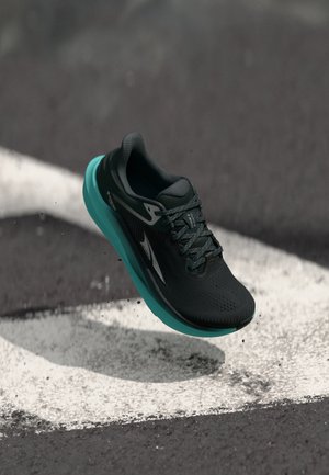 Black running shoe with a textured upper, teal midsole, and white accents, shown hovering above a contrasting surface.