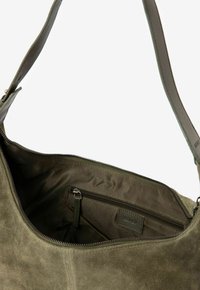 Sac à main en cuir suédé vert olive avec une ouverture zippée et une poche intérieure zippée. Design structuré avec un fond plat et une large bandoulière.