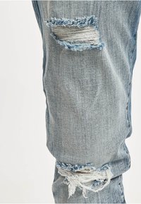 Lyseblå denimjeans med revne knær og frynsete kanter. Stoffet viser en strukturert veving med et avslappet, slitt utseende.