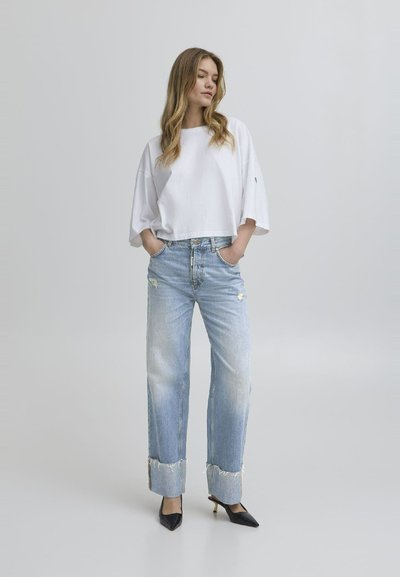 Weißes, kurzes T-Shirt mit weiten Ärmeln, hellblaue, ausgefranste Jeans mit fransigen Säumen und schwarze, spitze Pumps. Einfaches und lässiges Outfit.