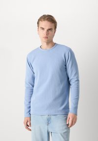 T-shirt a maniche lunghe di colore azzurro chiaro realizzato in tessuto testurizzato, con scollatura a girocollo e piccolo logo ricamato sul petto.